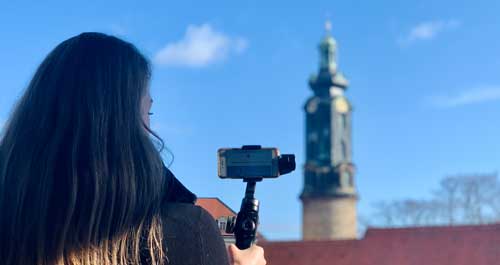 Online-Stadtführung Frau mit Handy und Denkmal im Hintergrund